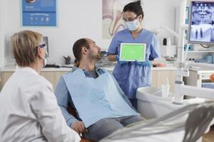 dentista donna Tenere finto su verde schermo croma chiave tavoletta con isolato Schermo discutere orale igiene con uomo paziente durante stomatologiche consultazione nel dentale ufficio. stomatologia concetto foto