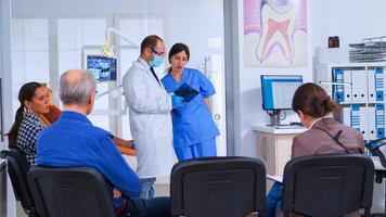 medico parlando con assistente Tenere denti raggi X in piedi nel in attesa camera di stomatologiche clinica prima pazienti visita medica, infermiera scrittura su computer, mentre medico andando nel consulenza ufficio. foto