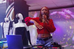 africano americano cantante l'esecuzione su palcoscenico a discoteca festa. donna dj cantando nel microfono e miscelazione brani con elettronico musica digitale stazione a club discoteca foto