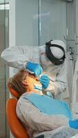 medico con protettivo maschera fare igienico pulizia di denti utilizzando sterile dentale utensili durante coronavirus pandemia. medico squadra indossare tuta, viso scudo, maschera, guanti nel stomatologiche clinica foto