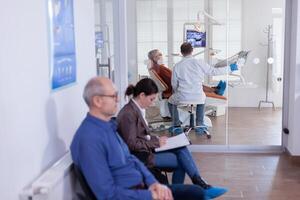 dentista con anziano paziente analizzando denti radiografia raggi X nel consultazione ufficio seduta su sedia. stomatologia corridoio con persone Riempimento trattamento appuntamento modulo. foto