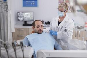 dentista anziano donna spiegando orale igiene per paziente con mal di denti durante odontoiatria visita medica nel stomatologiche ufficio camera. ortodontista medico Lavorando a denti infezione utilizzando trapano strumento foto