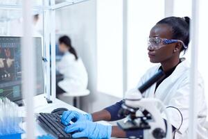 professionale africano medico lavoratore digitando informazione di virus studia nero assistenza sanitaria scienziato nel biochimica laboratorio indossare sterile attrezzatura. foto