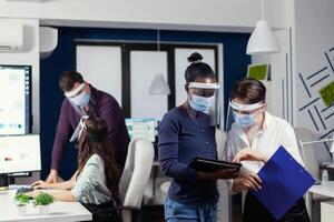 internazionale gruppo di persone Lavorando e comunicare in piedi a posto di lavoro indossare viso maschera contro covid19. multietnico attività commerciale squadra Lavorando rispetto sociale distanza durante globale pandemia con coronavirus. foto