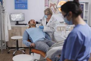 dentista medico donna con viso maschera utilizzando dentale utensili mentre controllo paziente bocca analizzando orale infezione durante stomatologiche consultazione nel odontoiatria ufficio camera. concetto di ortodontista squadra foto