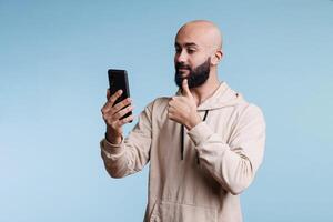 giovane arabo uomo mostrando pollice su mentre A proposito di nel video chiamata utilizzando smartphone. persona fabbricazione approvare cartello mentre avendo in linea a distanza conversazione nel mobile Telefono video conferenza foto