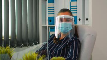 manager donna con visiera e protezione maschera guardare a telecamera sorridente nel nuovo normale attività commerciale ufficio. libero professionista Lavorando nel finanziario azienda rispetto sociale distanza durante globale pandemia. foto