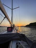 un' uomo è in piedi su il arco di un' barca a vela a tramonto foto