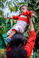 amorevole mamma trasporto di sua bambino a società parco. luminosa ritratto di contento mamma Tenere bambino nel sua mani. madre abbracciare sua poco 9 mesi vecchio figlio. foto