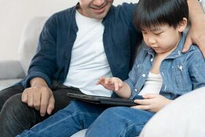 contento singolo padre giocando insegnare utilizzando tavoletta con il poco ragazzo. famiglia è contento e eccitato nel il Casa. padre e figlio avendo la spesa tempo insieme, bene papà , dipendenza aggiustare, maneggiare, controllo foto