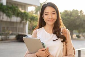 bellissimo alunno asiatico donna con zaino e libri all'aperto. Sorridi ragazza contento trasporto un' lotto di libro nel Università città universitaria. ritratto femmina su internazionale Asia Università. formazione scolastica, studia, scuola foto