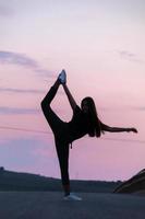 bella giovane ragazza bruna in posa di una strada in mezzo al campo al tramonto, balletto, silhouette foto