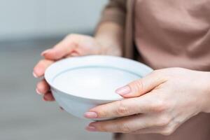 irriconoscibile donna Tenere vuoto ciotola nel sua mani, cucina interno, copia spazio, avvicinamento sparo, ritagliata di Affamato signora affamato. carestia, povertà, fame, crisi concetto foto