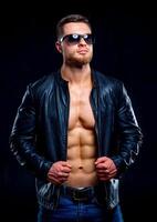macho uomo con Perfetto corpo nel occhiali da sole con Aperto pelle giacca rivelatrice muscolare il petto e torso. avvicinamento foto