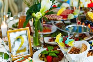 festosamente servito tavolo con diverso cibo, decorato con fiori per banchetto, ristorante interno. abbondanza di gustoso cibo per ospiti. foto