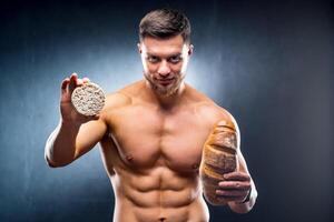 giovane nudo torso uomo Tenere cereale cracker e pane . la scelta fra salutare e dannoso cibo. orizzontale foto grigio sfondo. avvicinamento