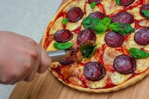 tagliare la pizza fatta in casa su un tagliere da cucina foto