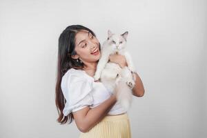 ritratto di giovane asiatico donna Tenere carino bambola di pezza gatto con blu occhi. femmina abbracciare sua carino lungo capelli gattino isolato di bianca sfondo. adorabile domestico animale domestico concetto. foto