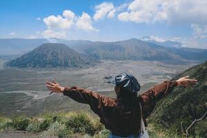 un asiatico ragazza in piedi su un' collina traccia nel bromo, godendo Visualizza di bromo, un' meraviglioso scenario nel drammatico collina foto