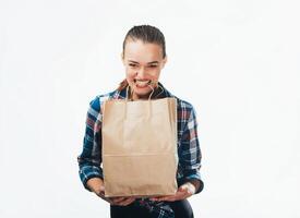 un' contento sorridente donna con un' shopping Borsa su un' bianca indietro. un' di bell'aspetto modello detiene il corde di shopping Borsa nel sua denti. foto