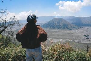 un asiatico ragazza in piedi su un' collina traccia nel bromo, godendo Visualizza di bromo, un' meraviglioso scenario nel drammatico collina foto