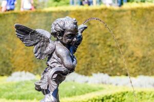 cherubino statua Fontana nel un' giardino con acqua flusso, soleggiato giorno sfondo. foto