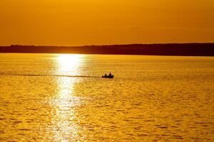 bellissimo tramonto sopra il grande lago o mare. tramonto spiaggia. arancia cielo. barca nel il mezzo di in profondità acqua. foto