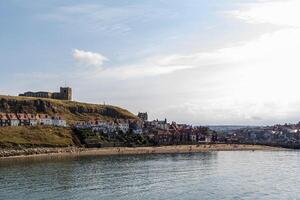 caratteristico costiero cittadina con colorato case di il mare, sotto un' chiaro cielo con morbido nuvole nel whitby, Inghilterra. foto