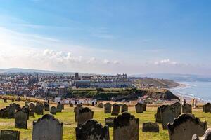 panoramico costiero cittadina visto a partire dal un' cima cimitero con Esposto alle intemperie lapidi, blu cielo, e mare nel il sfondo nel whitby, Inghilterra. foto