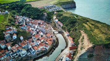 aereo Visualizza di un' caratteristico costiero villaggio con case annidato di un' fiume principale per il mare, circondato di verde scogliere nel staithes, Inghilterra. foto