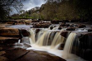 sereno cascata a cascata al di sopra di rocce con lussureggiante verdura nel il sfondo, in mostra della natura la tranquillità nel yorkshire valli. foto