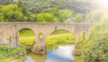 vecchio pietra ponte nel il verde foresta attraverso il fiume foto
