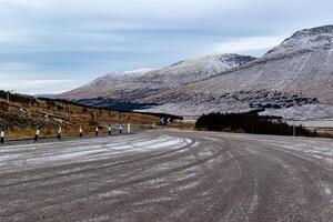 avvolgimento strada nel un' montagnoso paesaggio con snow-capped picchi e nuvoloso cieli. foto