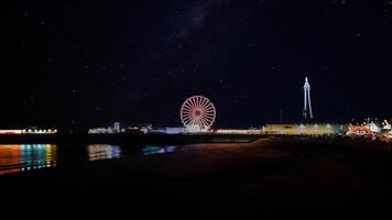 ore notturne costiero scena con illuminato Ferris ruota e faro, riflettendo su acqua con stellato cielo sfondo nel backpool, Inghilterra. foto