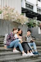 studenti siamo studiando il città universitaria parco. giovane persone siamo la spesa tempo insieme. lettura prenotare, Lavorando con computer portatile, tavoletta e comunicare mentre foto