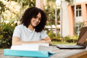 bellissimo alunno studiando su linea e apprendimento scrittura Appunti nel un' scrivania nel un' città universitaria. foto