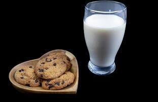 cioccolato patata fritta biscotti su un' cuore sagomato piatto con un' bicchiere di fresco latte su nero sfondo foto