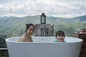 asiatico famiglia, mamma e bambino giocando insieme, senza fretta rilassare nel vasca da bagno, godere felicemente con panoramico montagna gamma Visualizza di tropicale paesaggio nel naturale scenario viaggio ricorrere per vacanza vacanza. foto