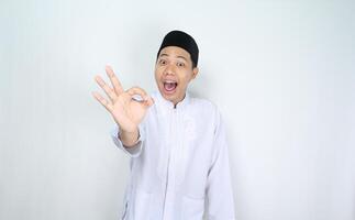 divertente musulmano uomo asiatico dare va bene segni con sorpreso espressione isolato su bianca sfondo foto