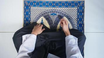 vista dall'alto dell'uomo musulmano con la mano in preghiera sul tappetino da preghiera mentre tiene i grani di preghiera foto