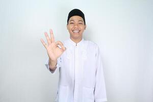 sorridente asiatico uomo musulmano mostrare ok segni isolato su bianca sfondo foto