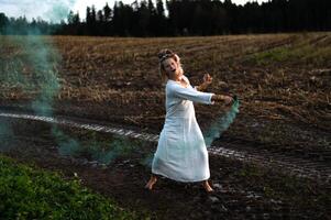 allegro giovane donna con canne balli nel colorato Fumo nel un' campo foto