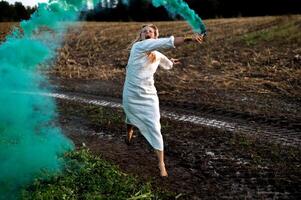 allegro giovane donna con canne balli nel colorato Fumo nel un' campo foto