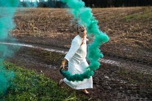 allegro giovane donna con canne balli nel colorato Fumo nel un' campo foto