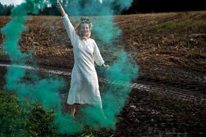 allegro giovane donna con canne balli nel colorato Fumo nel un' campo foto