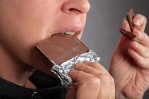 un' donna, il cui, di chi viso è non visibile, mangia un' cioccolato sbarra. foto