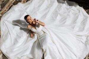 un' bellissimo sposa nel un' bianca vestito è dire bugie. un' ragazza nel un' bianca vestito è riposo. bellissimo capelli e trucco. il modello pose per il fotografo. foto