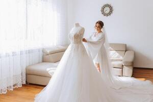 un' bellissimo sposa con un' lungo velo nel sua camera, indossare un' veste. nozze vestito su un' manichino. il sposa nel il mattina prima il nozze cerimonia. foto