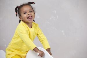 poco africano americano ragazza nel giallo Abiti Spettacoli lingua. divertente bambino. foto