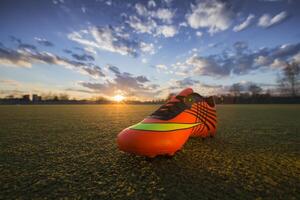 gli sport scarpe su il sfondo di il campo a tramonto. calcio campo con scarpe da ginnastica foto